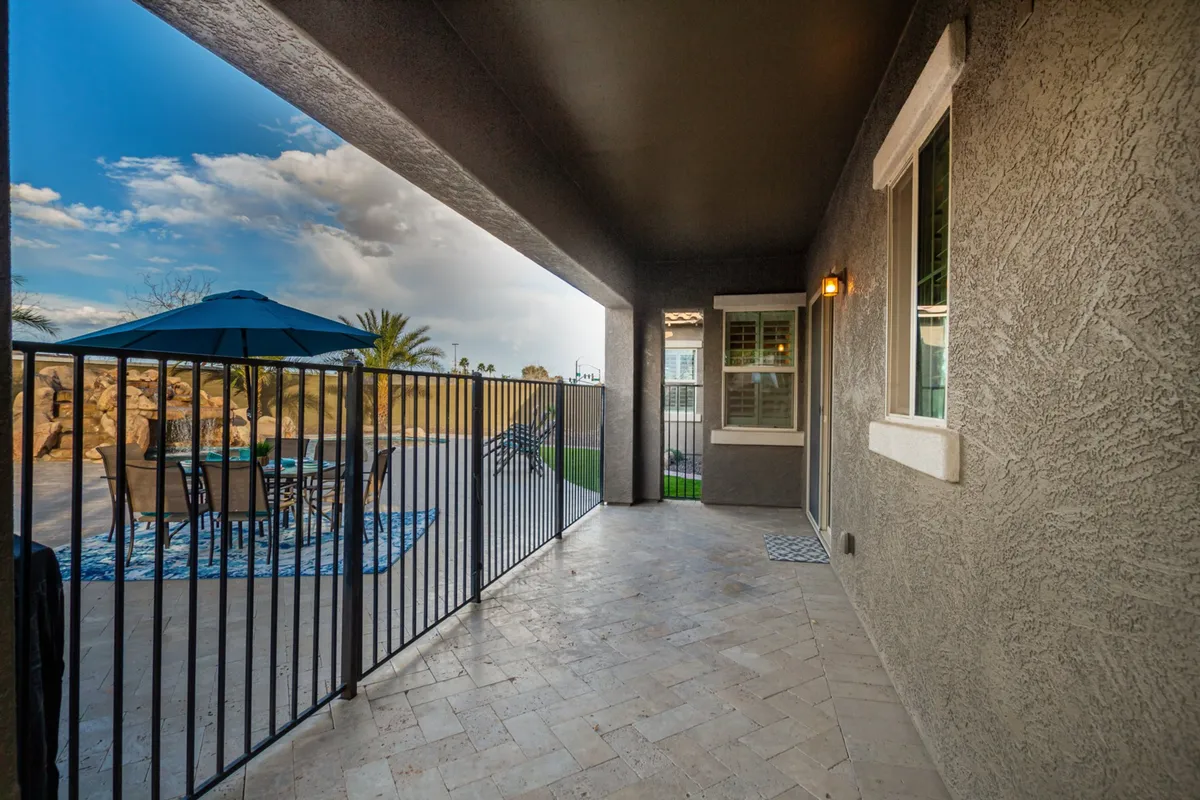 This image features a secure, fenced backyard patio area with comfortable patio furniture and an umbrella set up for alfresco dining. The space is clearly designed for multiple guests and provides a welcoming spot for all ages to relax outdoors.