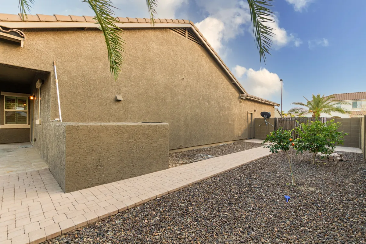 A serene exterior pathway bordered by lush green shrubbery and palm trees leads to the house. The tranquil garden-like setting evokes relaxation and outdoor enjoyment, hinting at sunset views and the inviting approach to the home.