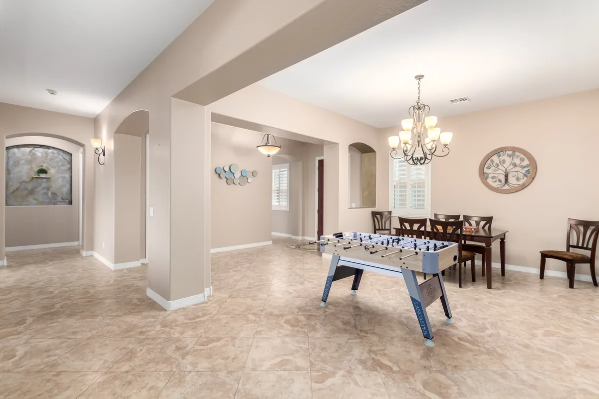 An interior scene showcasing a foosball table at the forefront, with a dining area, chandelier, and decorative wall art in the background. The space feels casual and lively, ideal for entertainment and gatherings, and is clearly part of an open-concept layout.