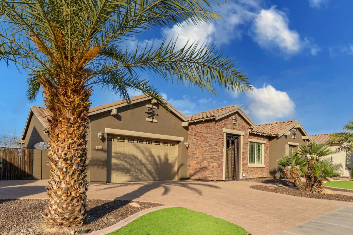 A welcoming exterior shot featuring the home's palm trees, stone facade, garage, and front entrance. The scene exudes an inviting mood, with soft lighting suggesting the potential for evening gatherings and a social atmosphere.