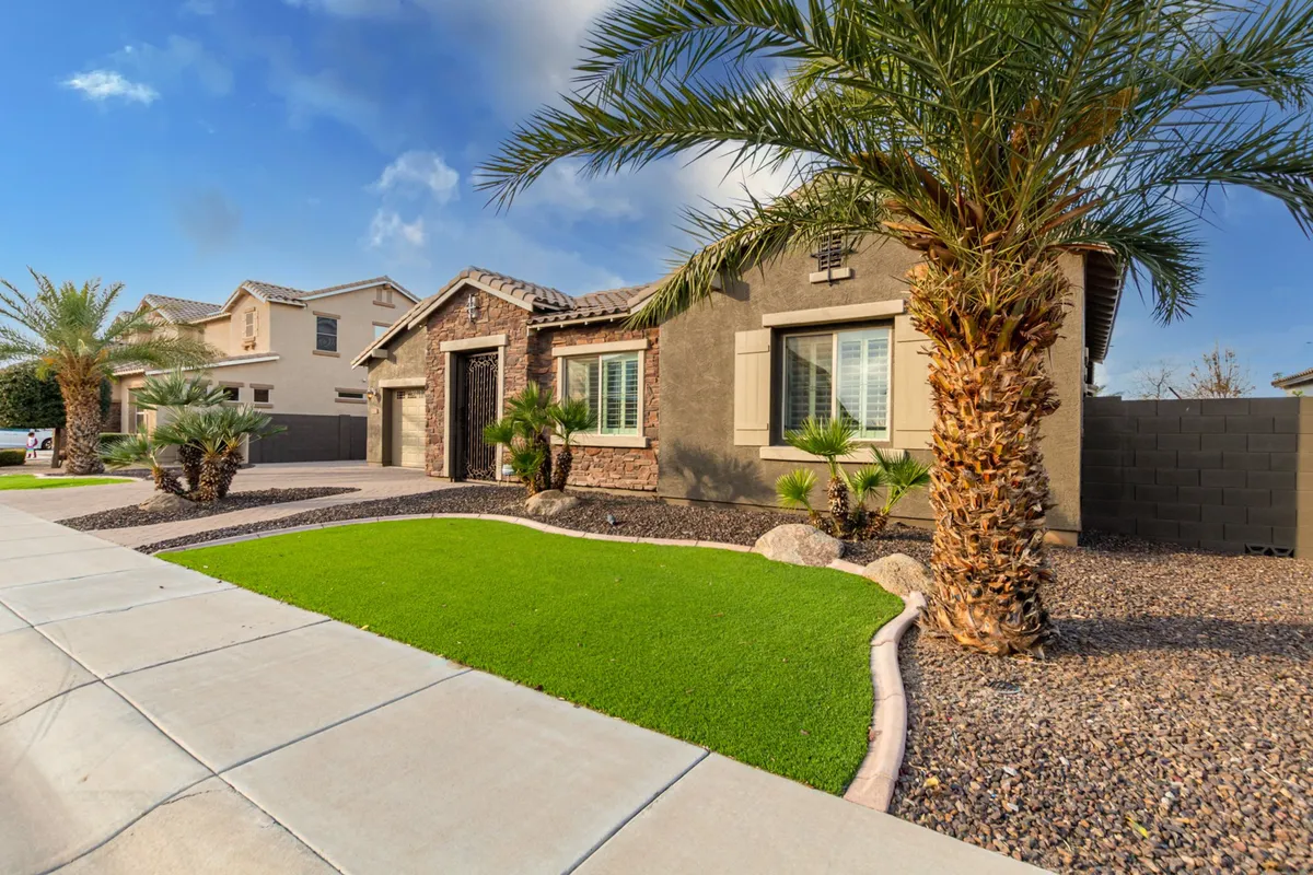 A view of the home's lush green lawn framed by tropical palm trees, with decorative stonework accenting the exterior. The setting is sunlit and showcases the welcoming, resort-like aura of the property, inviting outdoor relaxation and gatherings.