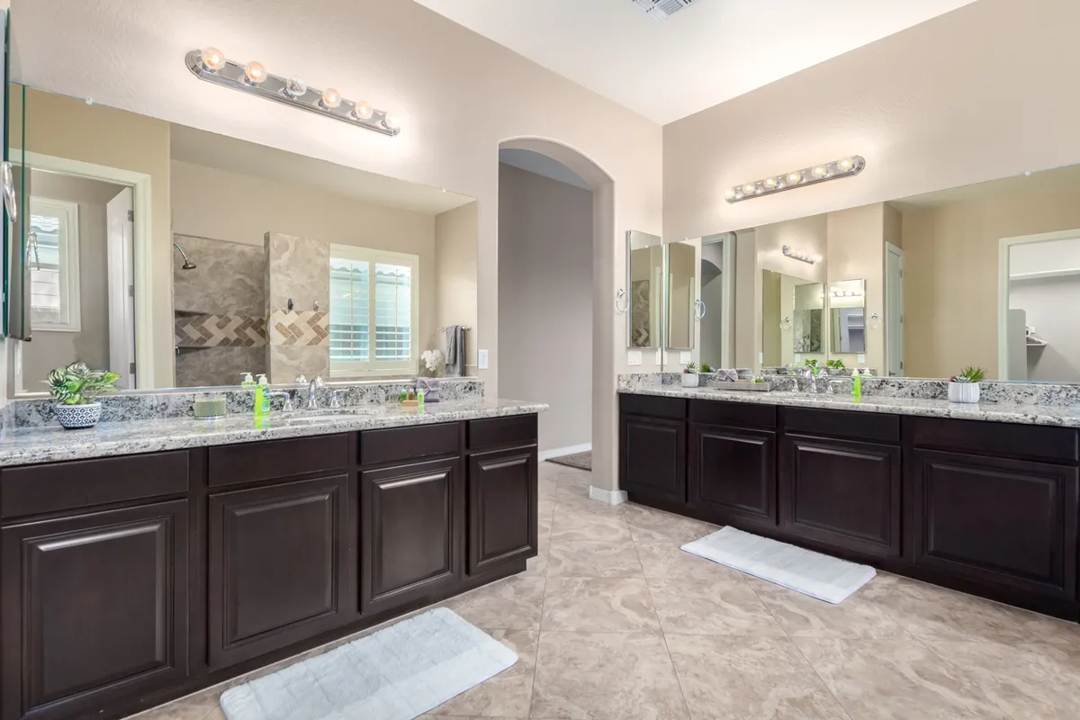 A bright, organized bathroom featuring double sink vanities with granite countertops and large mirrors, evoking a sense of daily luxury and comfort.