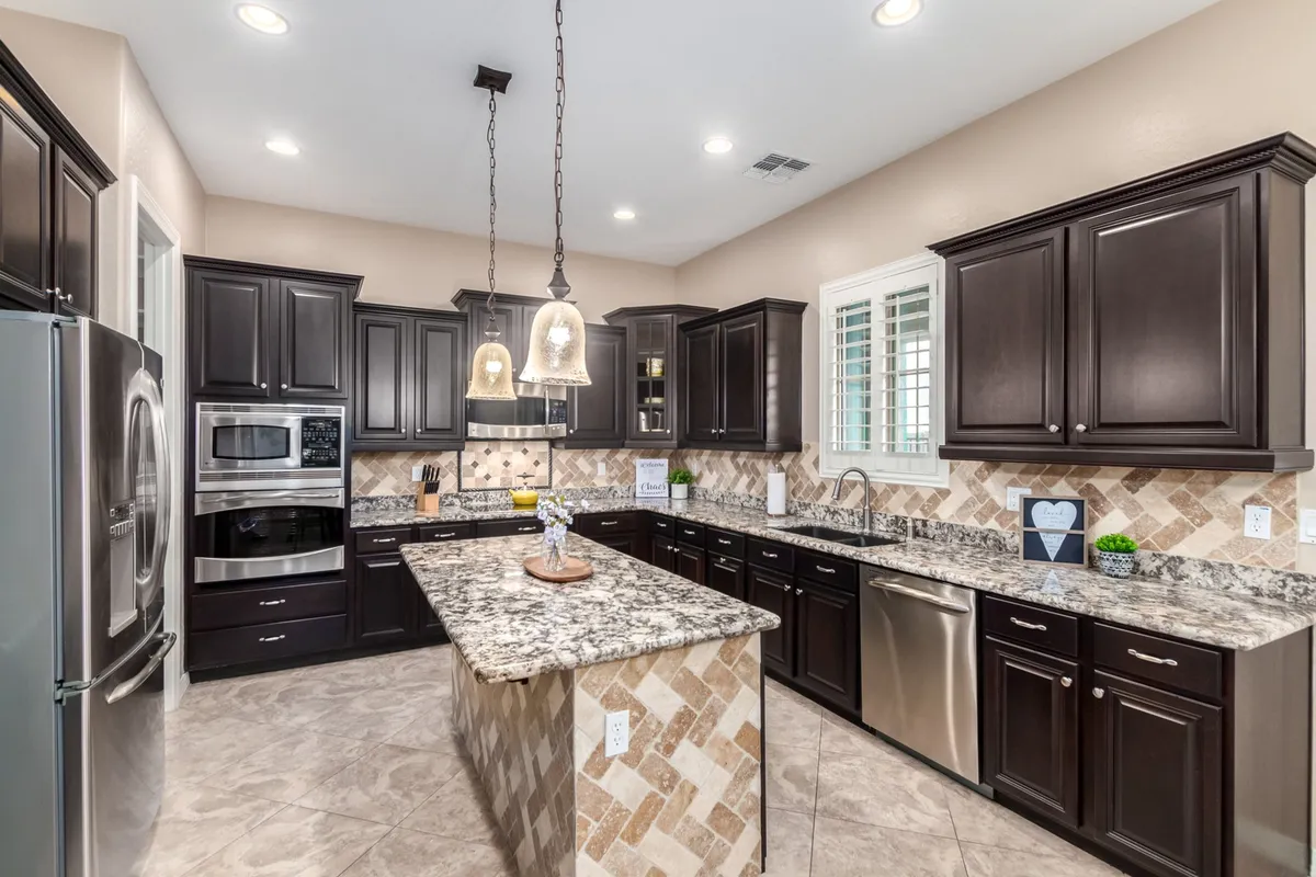 Inside the spacious chef’s kitchen, granite countertops gleam beneath modern pendant lights. Dark wooden cabinetry and an expansive kitchen island invite gourmet meal preparation and entertaining in a setting that is both functional and elegant.