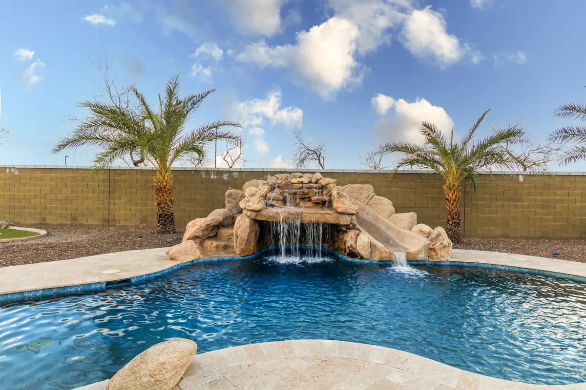 A serene outdoor scene with a swimming pool, waterfall feature, and lush palm trees. The pool area is inviting for both children playing and adults lounging, offering a peaceful yet playful environment.