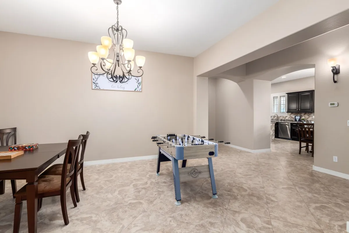 A bright, lively interior scene with a dining table ready for meals and a foosball table nearby. The chandelier adds a festive touch, and the space hints at memorable group activities like game nights and shared dinners.