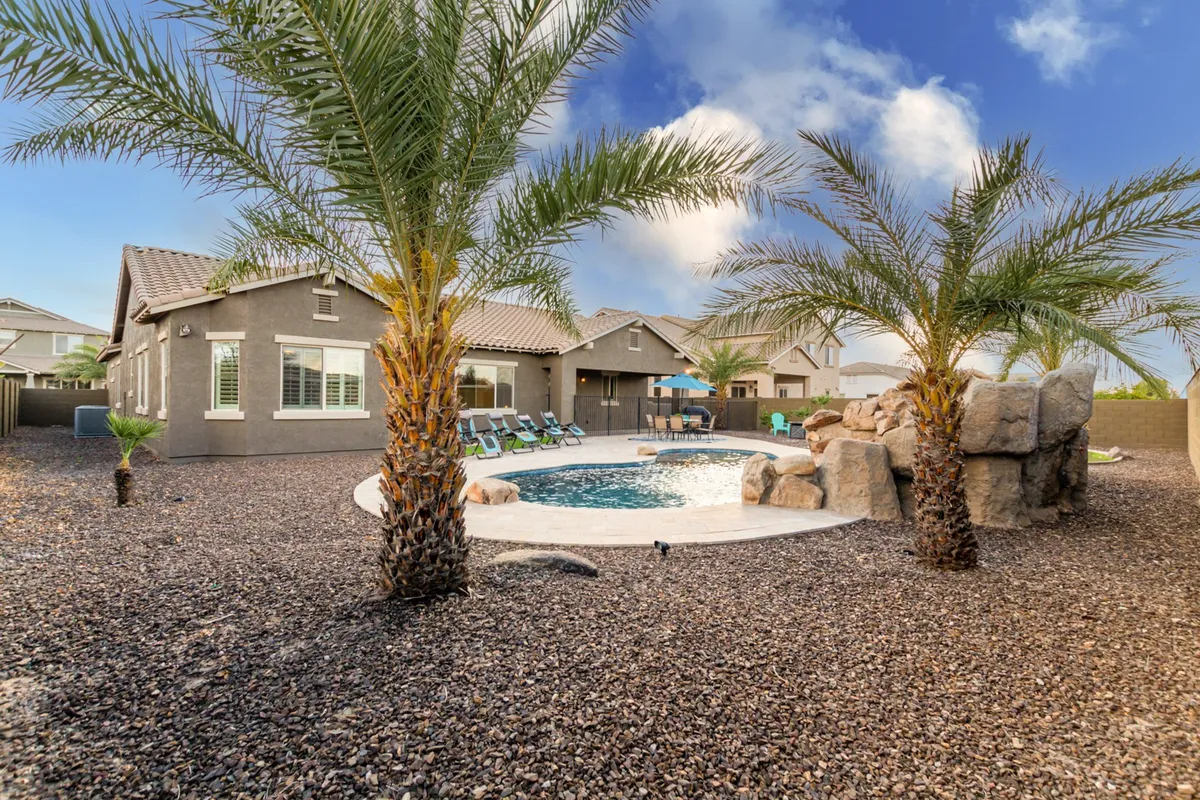 A stunning outdoor scene featuring a sparkling swimming pool alongside palm trees and natural rock features. Comfortable lounge chairs are positioned to take in the tranquil views, inviting guests to relax and soak up the Arizona sun. The pool area exudes a resort-like atmosphere perfectly suited for swimming, sunbathing, and memorable poolside gatherings.