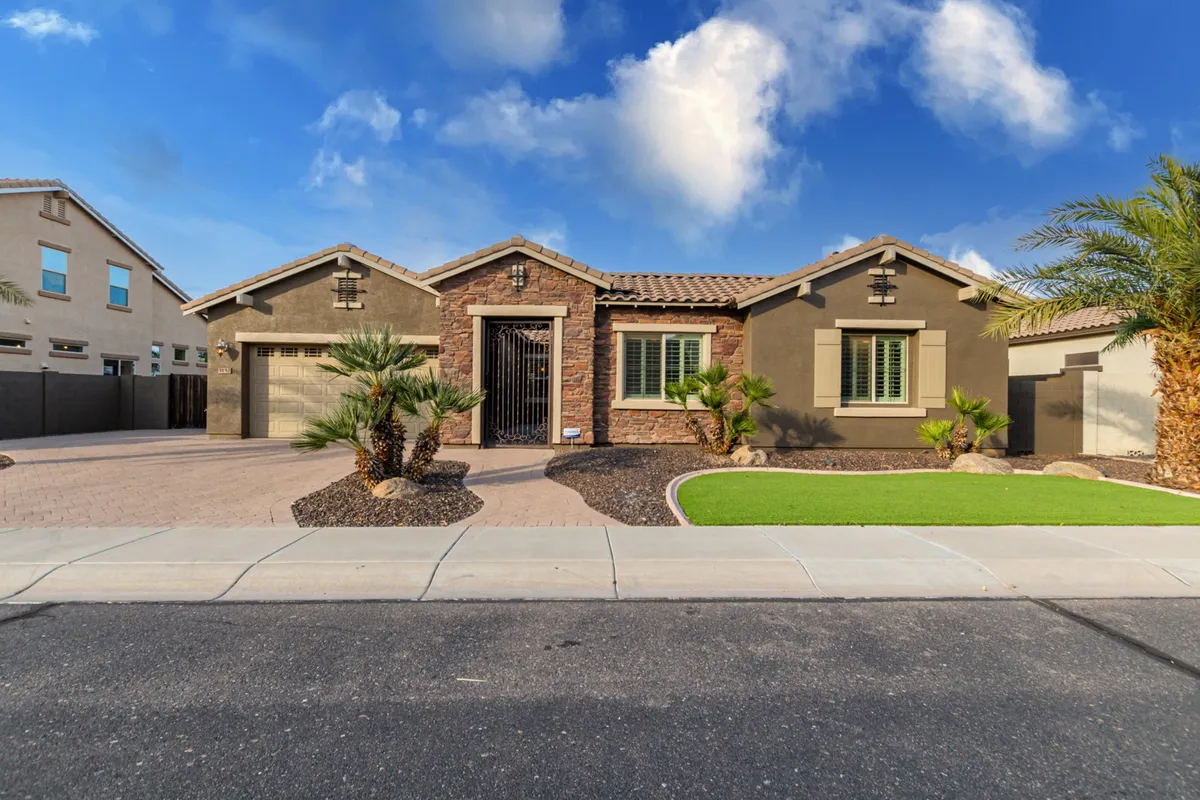 A wide shot of the property’s stone façade and front gate, shaded by mature palm trees and bordered by a meticulously landscaped yard. The inviting entrance hints at privacy and exclusivity, welcoming guests into a high-end retreat.