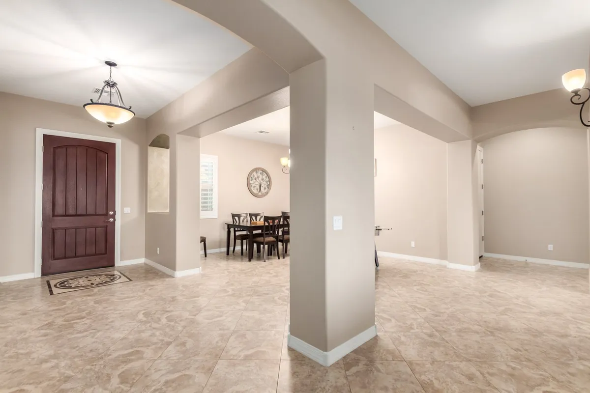 A stylish, airy dining area with arched doorways and a wooden front door, seamlessly blending the transition from welcoming guests at the entrance to gathering for a meal. The open layout emphasizes social connection and celebration.