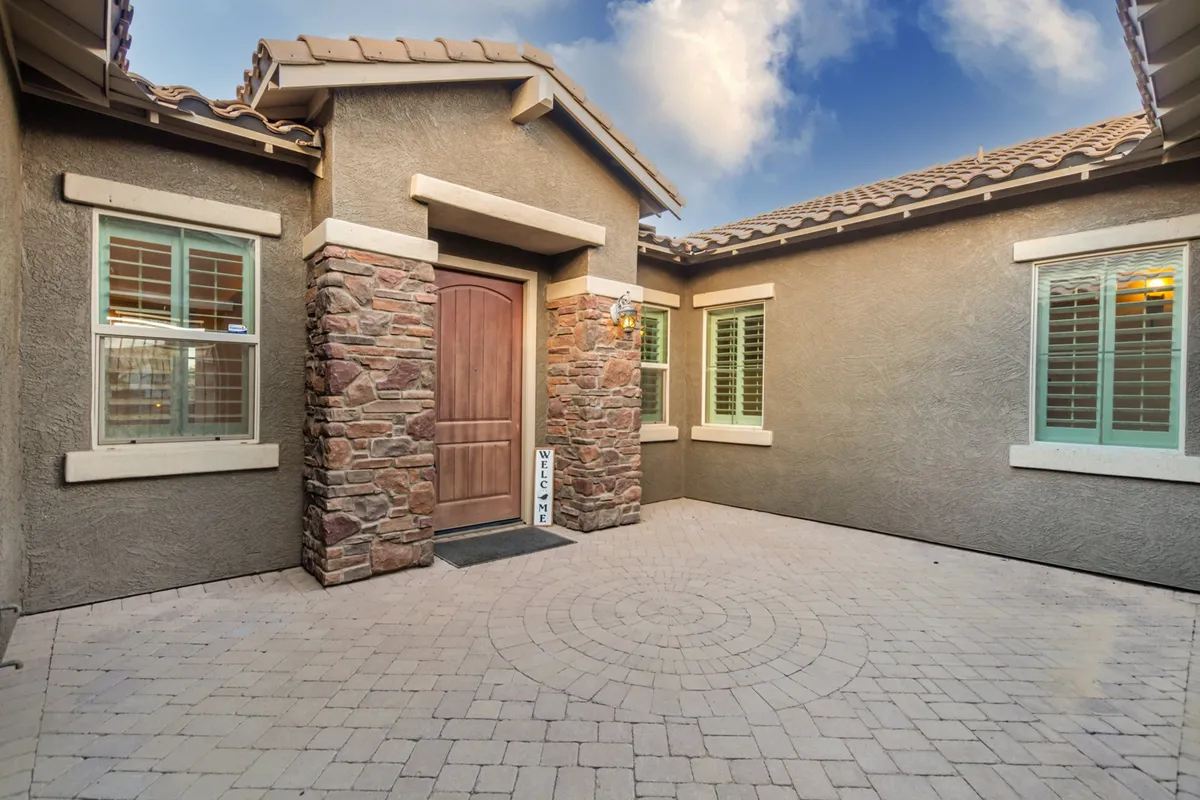 This image captures the wooden front door framed by a textured stone facade and a paved courtyard. The scene is bright and welcoming, featuring a spacious entry with an inviting atmosphere, ideal for creating a strong first impression of the home. The courtyard is visible, suggesting a transition from outside to inside.